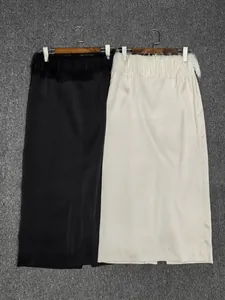 Detail of satin midi skirts in black and beige featuring feather tassel waist accents