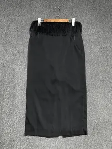 Detail of a black satin maxi skirt with decorative fringe tassels at the waistline
