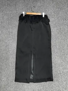 Detail of black satin skirt featuring dense fringe waist and elegant front slit