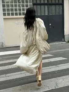 Rear view of loose beige long-sleeved dress with puff sleeves and pleated hem on street