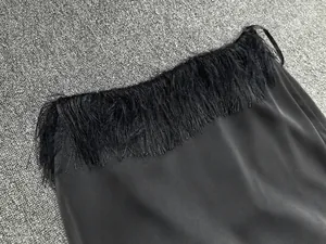 Detail of elegant black satin fabric skirt featuring luxurious soft tassel trim at the hem