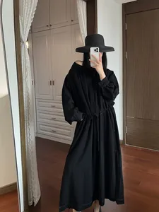 Detail of black long-sleeve dress featuring white contrast stitching and waist tie belt