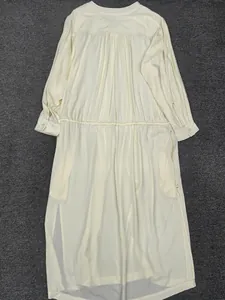 Detail of gathered waist and buttoned cuffs on a minimalist cream long sleeve dress