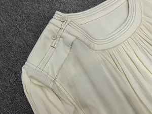 Detailed view of cream-colored off-shoulder dress with pleated neckline and button accents