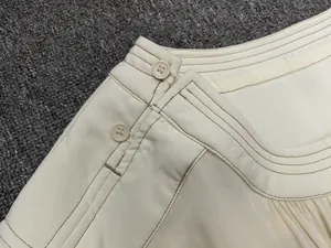 Detailed view of cream-white dress waist featuring resin buttons and brown contrast stitching