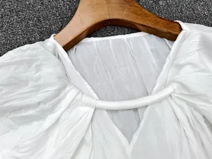 Detail of white V-neck top with pleated texture and decorative bar on a wooden hanger