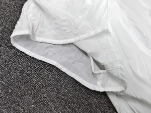Detailed close-up showing the double-stitched hem and textured fabric of the white top