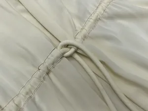 Detail of off-white satin dress showing refined pleats and drawstring knot texture