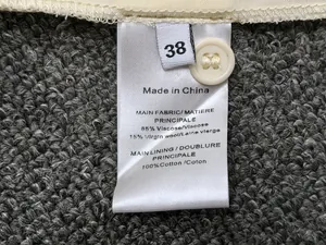 Detail of fabric care label with size 38 and spare button on gray textured wool blend fabric