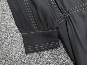 Detail of black long sleeve dress featuring white contrast stitching and pleated cuffs