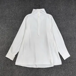 Detail view of white loose long sleeve shirt featuring high collar and back button placket
