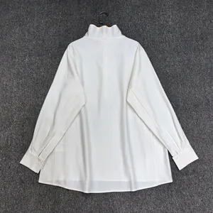 Flat lay of loose white high-neck cotton blouse back view on dark textured background