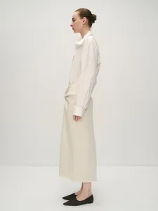 Side view of white long-sleeve cotton shirt paired with beige wrap-around maxi skirt