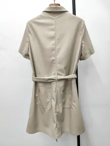 Detail eines beigen Kunstleder-Kleides mit Reverskragen, Gürtel und aufgesetzten Taschen
