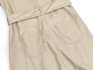 Detail eines cremefarbenen Lederkleides mit Gürtel und symmetrischen Rückentaschen