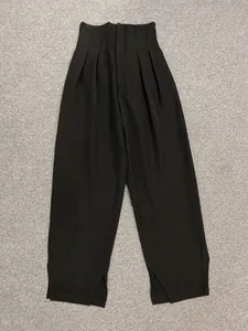 Detail of high-waist black wide-leg pants with pleated waist and side slit at the hem