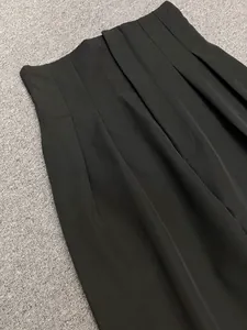 Detail of high waist black wide-leg trousers showing pleated front and smooth texture