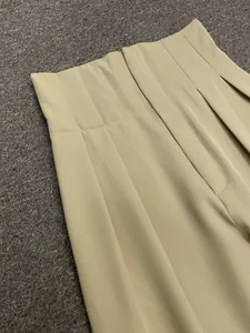 Detail of high-waist beige trousers showing intricate pleat design and premium draping fabric