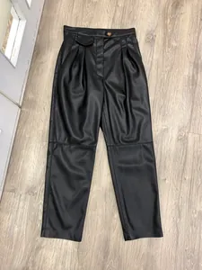 Detail view of high-waist matte black faux leather trousers with brown tortoiseshell button