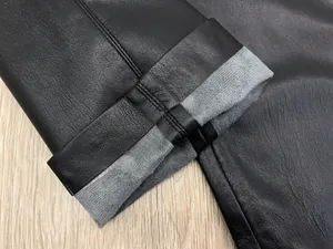 Detailed macro view of black faux leather pants showing warm grey fleece lining and dual stitching