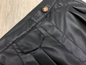 Detail view of high-waisted black leather pants with amber button and pocket stitching
