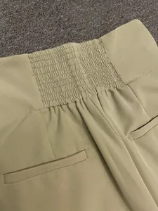 Detail of high-waist khaki trousers featuring smocking elastic waistband and piped pockets