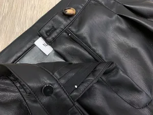 Detail view of black faux leather pants featuring pleats and a marble button closure