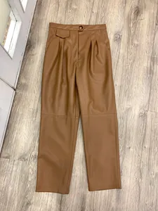 Detail of high-waist brown faux leather pants with pleated waist and knee seam stitching