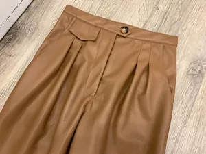 Detail of high waist pleated brown faux leather pants with tortoiseshell button