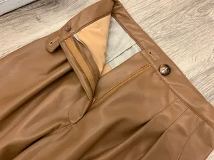 Detail view of caramel brown faux leather trousers featuring zipper and amber button