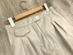 Detail of high-waist cream PU leather trousers with decorative pocket and pleats