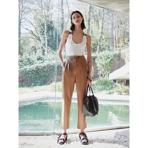 Women's high-waisted pleated leather straight-leg pants in brown standing by a pool