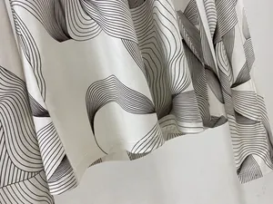 Détail du tissu ivoire avec motifs ondulés noirs et finition soignée à double couture