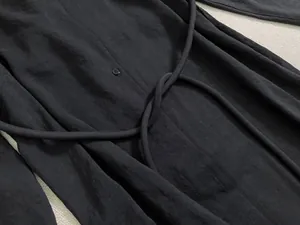 Détail de la texture de la robe chemise noire avec bouton et nœud de ceinture en corde
