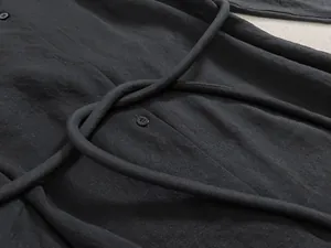Vue détaillée du tissu noir avec plis texturés et bouton sur robe chemise à manches