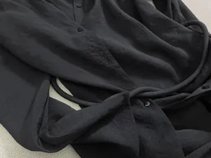 Détail d'une robe chemise noire à manches longues avec patte de boutonnage et ceinture nouée