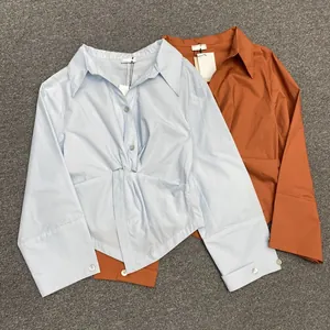Detail of twisted waist knot and asymmetric hem on long-sleeved button-up shirts