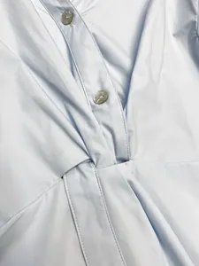 Detail of light blue shirt featuring a V-neck, waist knot design and pearl shell buttons