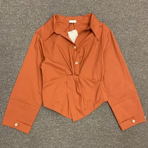 Detail view of the orange long-sleeved shirt with elegant front knot and pleats