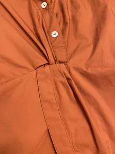 Close-up of burnt orange top featuring shell buttons and intricate knotted fold details