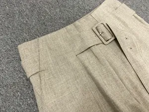 Detail of high-waist pleated trousers featuring textured fabric and a matching waist belt