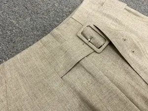 Detail of oat-colored high waist trousers featuring textured fabric and matching square buckle
