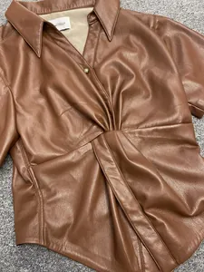 Detail of dark brown leather shirt showing twisted waist design and vintage metal buttons