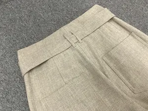 Detail of high-waist linen trousers featuring a matching belt and square back pockets