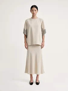 Detail of loose beige knit top with black striped cuffs and matching A-line skirt