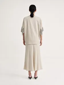 Detail of minimalist beige short sleeve top with black stripe accent on cuff and midi skirt