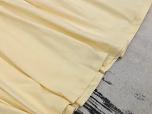 Détail macro de l'ourlet d'une robe jaune crème montrant coutures fines et plis doux