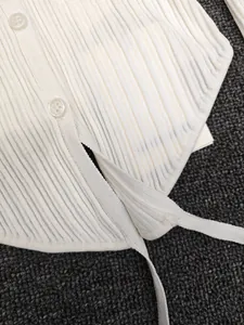 Detailed view of white ribbed knit cardigan with buttons and hem tie-up design