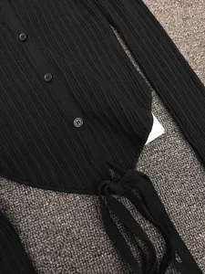Detail of black ribbed knit cardigan featuring button closure and self-tie hem bow