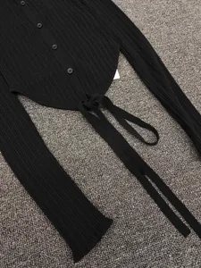 Detail of black ribbed knit cardigan featuring button closure and adjustable tie-up hemline